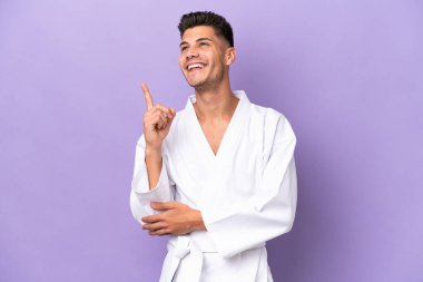 Mor arka planda karate yapan genç beyaz adam harika bir fikre işaret ediyor.