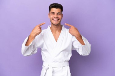 Mor arka planda karate yapan genç beyaz bir adam baş parmak hareketi yapıyor.