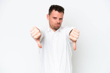 Beyaz arka planda soyutlanmış beyaz tenli yakışıklı bir adam baş parmağını iki eliyle aşağı gösteriyor.