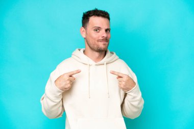 Mavi arka planda soyutlanmış beyaz tenli yakışıklı bir adam kendini işaret ediyor.