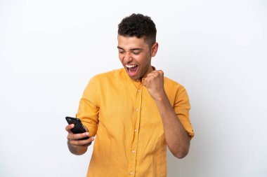 Beyaz arka planda telefonu zafer pozisyonunda olan beyaz Brezilyalı genç adam.