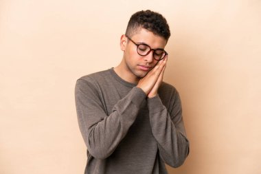 Genç Brezilyalı bir adam bej arka planda izole edilmiş bir şekilde uyku jesti yapıyor.