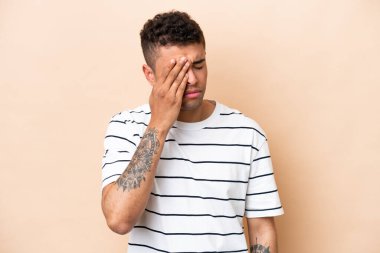 Young Brazilian man isolated on beige background with headache