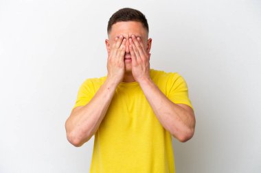 Genç Brezilyalı bir adam beyaz arka planda izole edilmiş, gözleri elle kapatılmış.