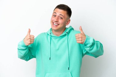 Beyaz arka planda izole edilmiş genç Brezilyalı bir adam baş parmak hareketi yapıyor.