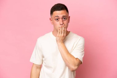 Pembe arka planda izole edilmiş genç Brezilyalı adam ağzını eliyle kapatıyor.