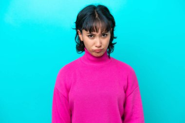 Arjantinli genç bir kadın üzgün bir ifadeyle mavi arka planda izole edilmiş.