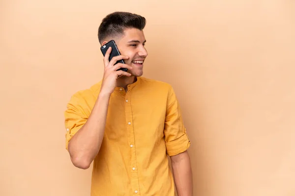Молодий Білий Чоловік Ізольований Бежевому Фоні Тримаючи Розмову Мобільним Телефоном — стокове фото
