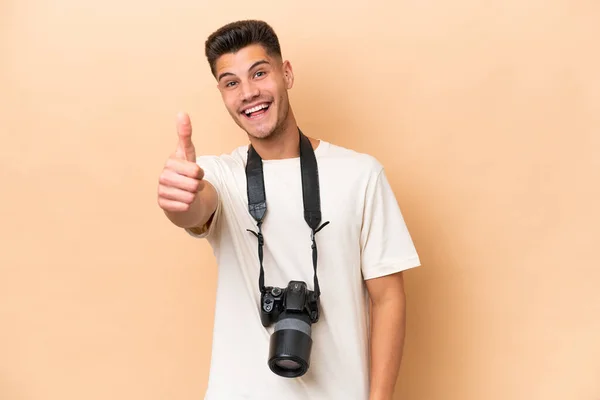年轻的摄影师高加索人 背景是米黄色的 大拇指竖起 因为发生了一些好事 — 图库照片