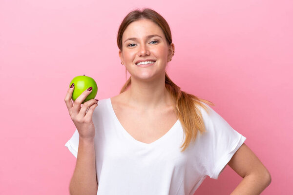 Young caucasian woman isolated on pink background with an apple and happy