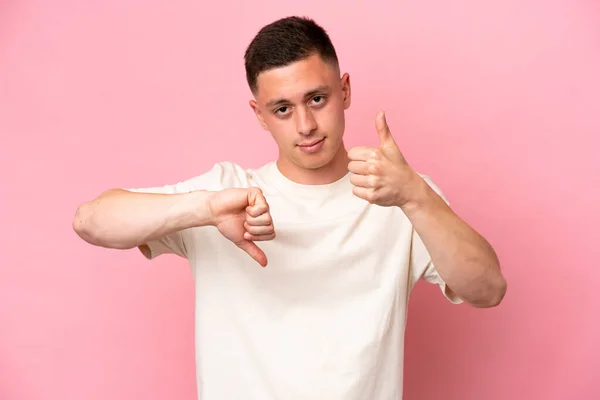 Young Brazilian man isolated on pink background making good-bad sign. Undecided between yes or not