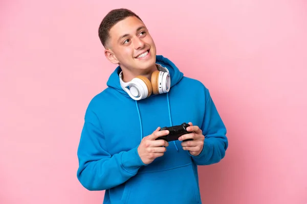 一个年轻的巴西男人在玩一个被粉色背景隔离的电子游戏控制器 一边抬头一边思考着一个想法 — 图库照片