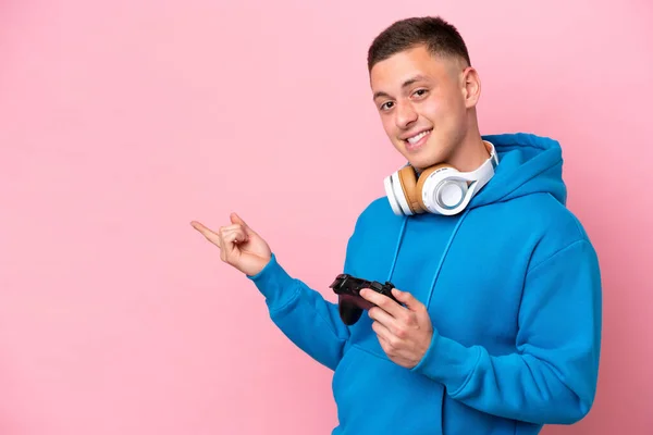 一个年轻的巴西男人在玩一个用粉色背景隔离的电子游戏控制器 手指指向旁边 — 图库照片
