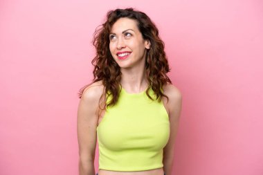 Pembe arka planda izole edilmiş genç beyaz kadın yukarı bakarken bir fikir düşünüyor.