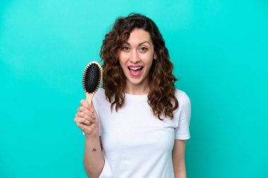 Mavi arka planda saç fırçası tutan beyaz bir kadın. Şaşırmış ve şok olmuş bir yüz ifadesi var.