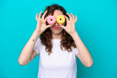 Mavi arka planda soyutlanmış beyaz bir kadın üzgün bir ifadeyle donut tutuyor.