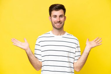 Sarı arka planda izole edilmiş genç beyaz adam şok olmuş yüz ifadesi ile