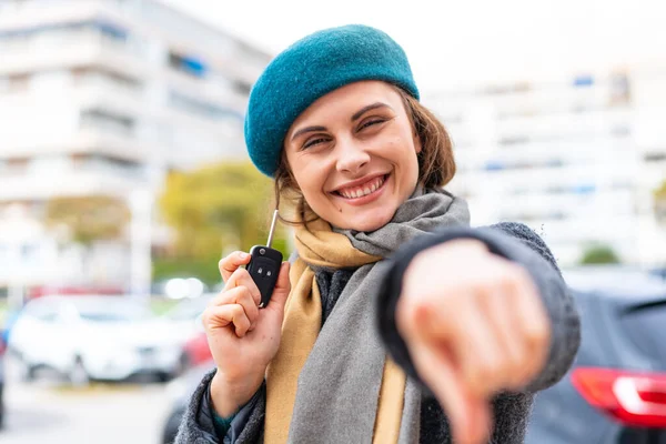 Brunette woman holding car keys at outdoors points finger at you with a confident expression