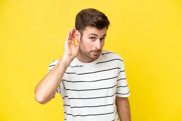 耳に手を置くことによって何かを聞く黄色の背景に隔離された若い白人男性 — ストック写真