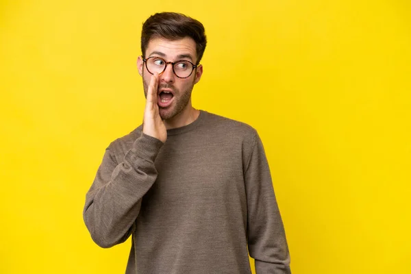 Young Caucasian Man Isolated Yellow Background Whispering Something Surprise Gesture — Stockfoto