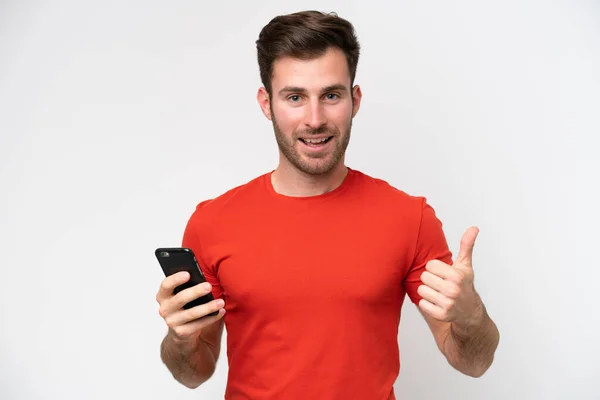 年轻的白人男子在竖起大拇指的时候用手机隔离在白色背景下 — 图库照片