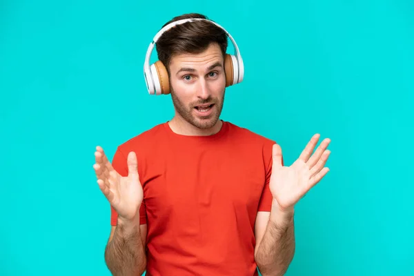 Jonge Blanke Man Geïsoleerd Blauwe Achtergrond Verrast Luisteren Muziek — Stockfoto