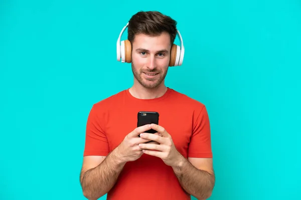 Young Caucasian Man Isolated Blue Background Listening Music Mobile Looking — Stock Photo, Image