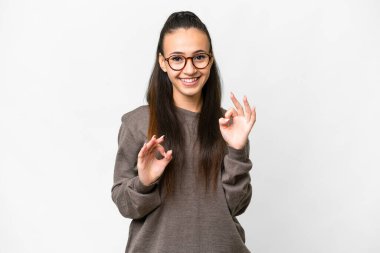 İzole edilmiş beyaz arka plan üzerinde genç bir Arap kadın iki eliyle tamam işareti gösteriyor.