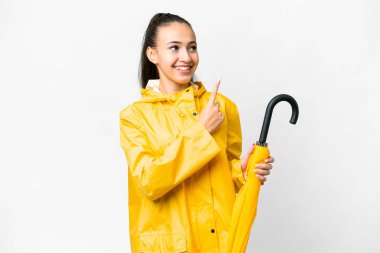 Yağmura dayanıklı ceketi ve şemsiyesi olan genç bir Arap kadını izole edilmiş beyaz arka planı harika bir fikre işaret ediyor.