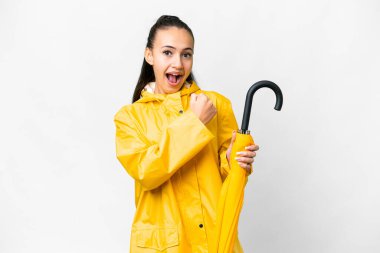 Yağmura dayanıklı ceketi ve şemsiyesi olan genç bir Arap kadını izole edilmiş beyaz arka planda zaferi kutluyor.