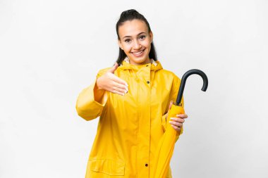 Yağmura dayanıklı ceketi ve şemsiyesi olan genç bir Arap kadın izole edilmiş beyaz arka planda iyi bir anlaşma için el sıkışıyor.