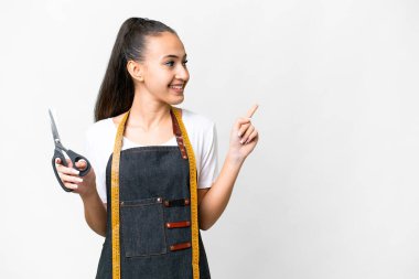 İzole edilmiş beyaz arka planda genç bir terzi kadın parmak işareti yapıyor ve bir ürün sunuyor.