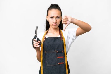 İzole edilmiş beyaz arka planda genç bir terzi kadın olumsuz bir ifadeyle baş parmağını aşağı gösteriyor.