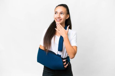 Kırık kollu genç bir Arap kadın ve izole edilmiş beyaz arka planda askısı var gülümserken yukarı bakıyor.