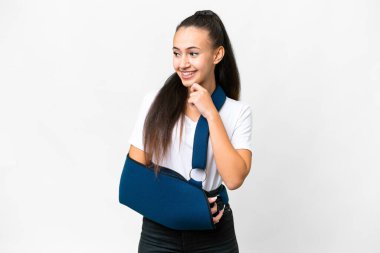 Kırık kollu genç bir Arap kadın izole edilmiş beyaz arka planda askısı var. Yan tarafa bakıyor ve gülümsüyor.