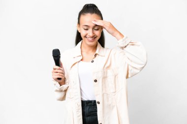 Genç şarkıcı kadın, izole edilmiş beyaz arka planda bir mikrofonu kaldırıp gülüyor.