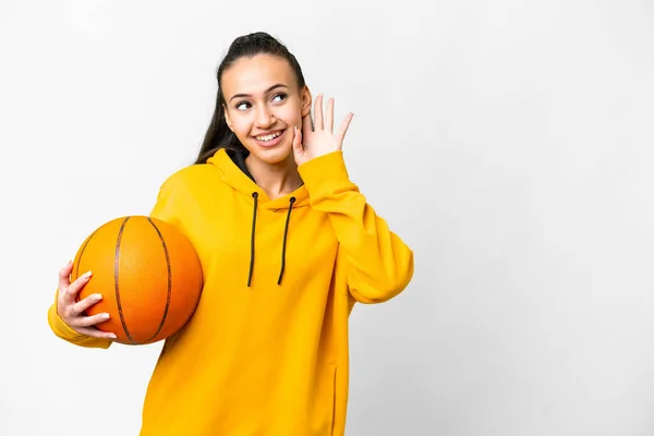 若いですアラビア人女性プレーバスケットボール上の隔離された白い背景は耳に手を置くことによって何かを聞く — ストック写真