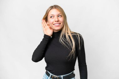 Young pretty blonde woman over isolated white background listening to something by putting hand on the ear