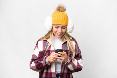 Young pretty blonde woman wearing winter muffs over isolated white background sending a message with the mobile