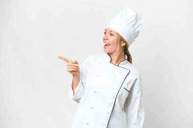 İzole edilmiş beyaz arka planda genç bir aşçı kadın parmak göstererek bir ürün sunuyor.
