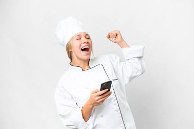 Genç aşçı kadın izole edilmiş beyaz arka planda telefon zafer pozisyonunda.