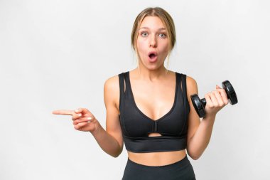 Sarışın sporcu kadın izole edilmiş beyaz arka plan üzerinde ağırlık kaldırıyor. Şaşırmış ve işaret ediyor.