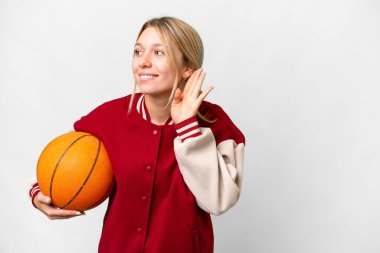 Basketbol oynayan genç sarışın bir kadın. İzole bir arka planda. Kulağına elini sürerek bir şeyler dinliyor.