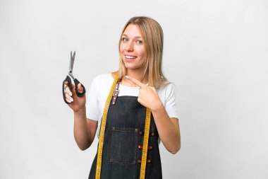 İzole edilmiş beyaz arka planı olan genç sarışın terzi kadın bir ürünü sunmak için kenarı işaret ediyor.