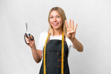 İzole edilmiş beyaz arka planda genç sarışın terzi kadın mutlu ve parmaklarıyla dörde kadar sayıyor.