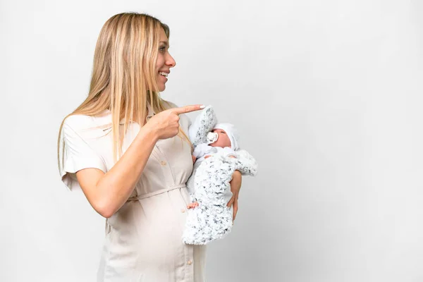 若いですかわいいです妊娠中の女性とともに彼女の新生児上の隔離された白い背景を指す側に製品を提示 — ストック写真
