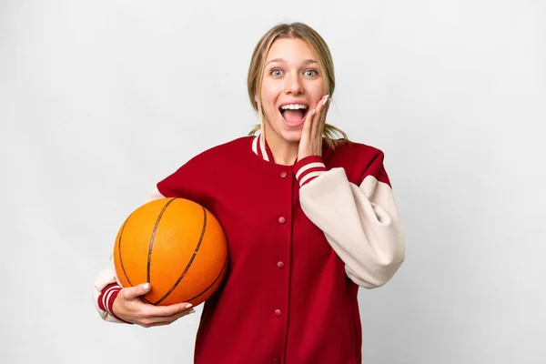 若いですブロンド女性遊びバスケットボール上の隔離された背景とともに驚きとショックを受けた顔の表情 — ストック写真