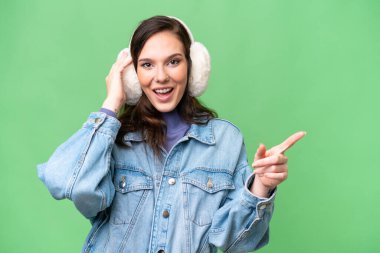 İzole edilmiş arka planda kışlık kuklalar takan genç beyaz kadın şaşırdı ve parmağını kenarı işaret etti.