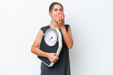 Genç, güzel Uruguaylı bir kadın beyaz arka planda, tartı makinesi ve elma ile izole edilmiş.