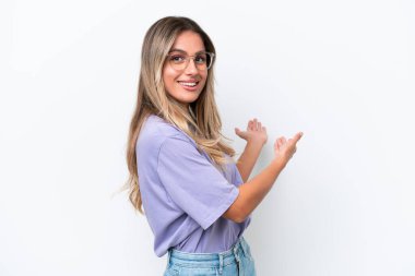 Genç Uruguaylı kadın, beyaz arka planda izole edilmiş, davet edilmek için ellerini yana uzatıyor.